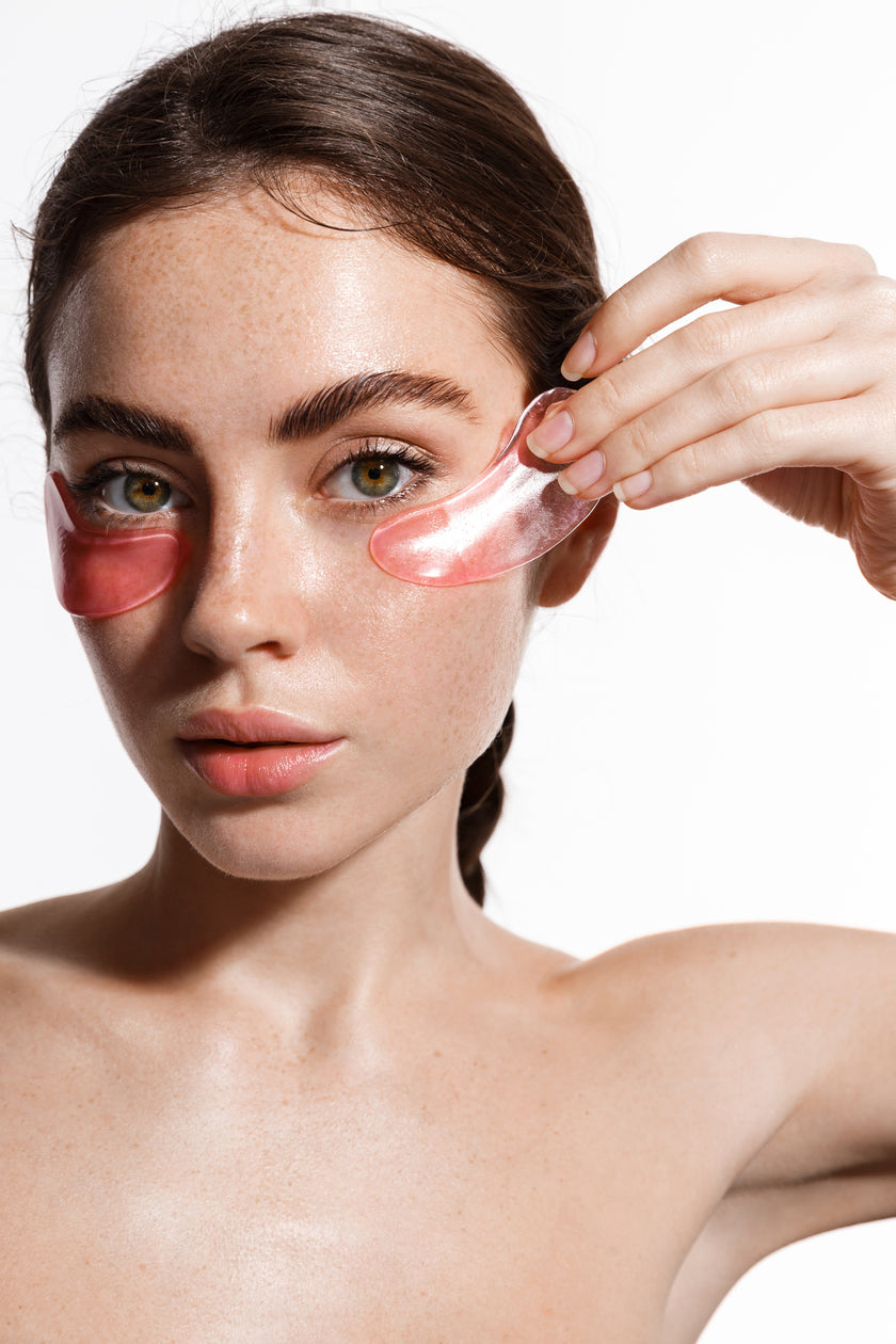Vertical beauty shot of young model with clean hydrated, moisturized skin using under eye patches mask with hyaluronic anti aging effect, treating puffiness and dark circles, white background 